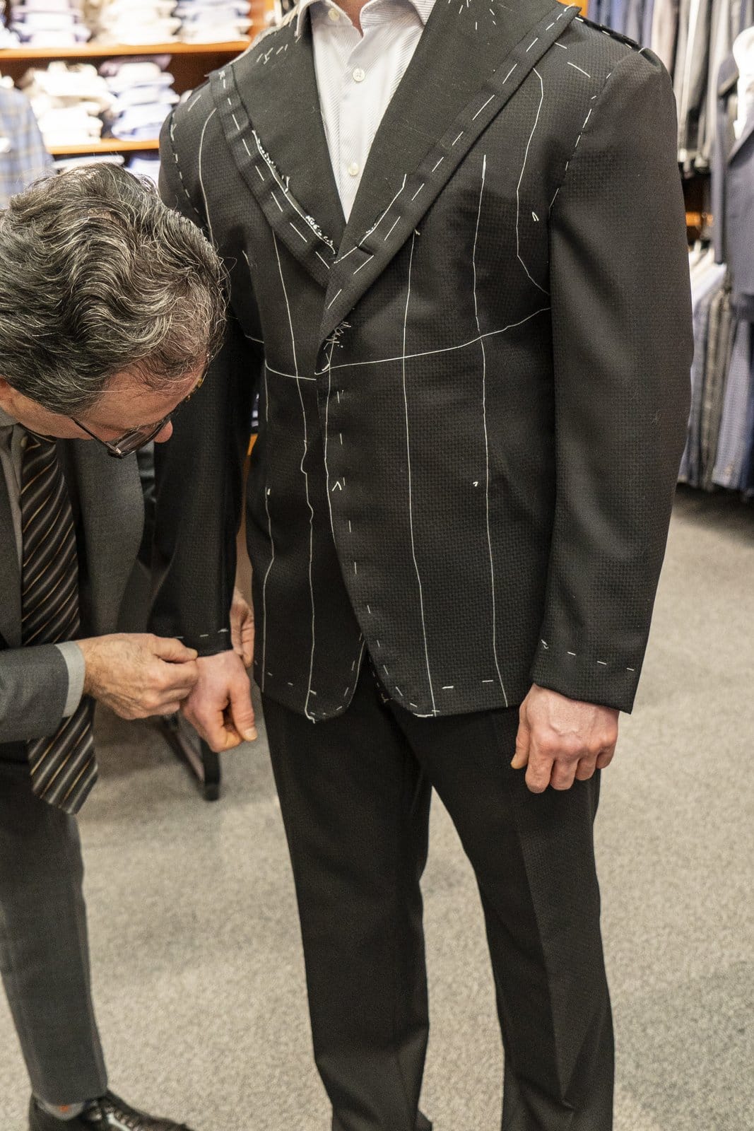 Tailor adjusting a dark jacket with visible basting stitches.