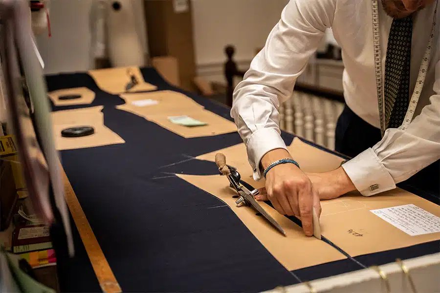 Tailor working with paper patterns on dark suiting fabric.